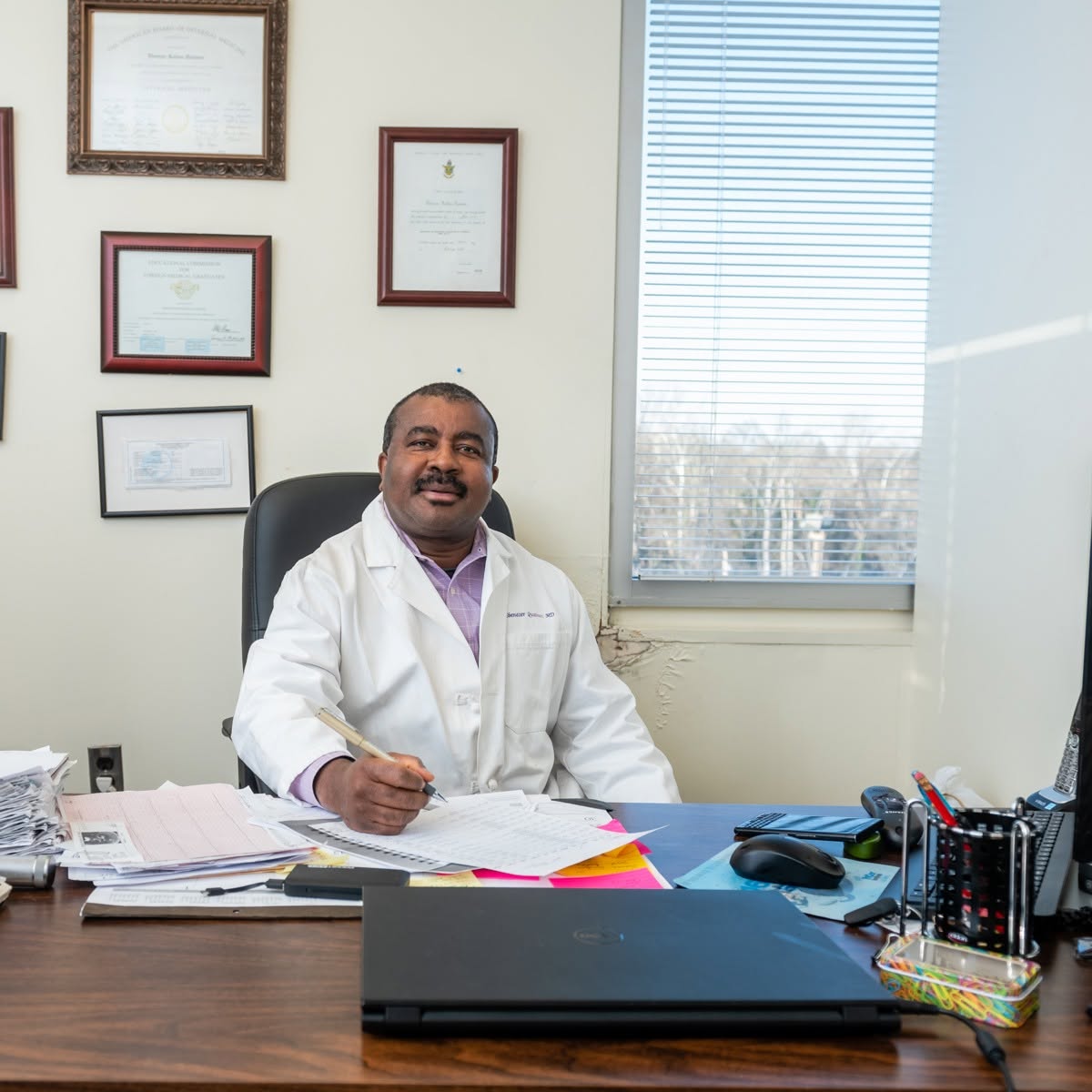 Doctor sitting at a desk with framed certificates on the wall.